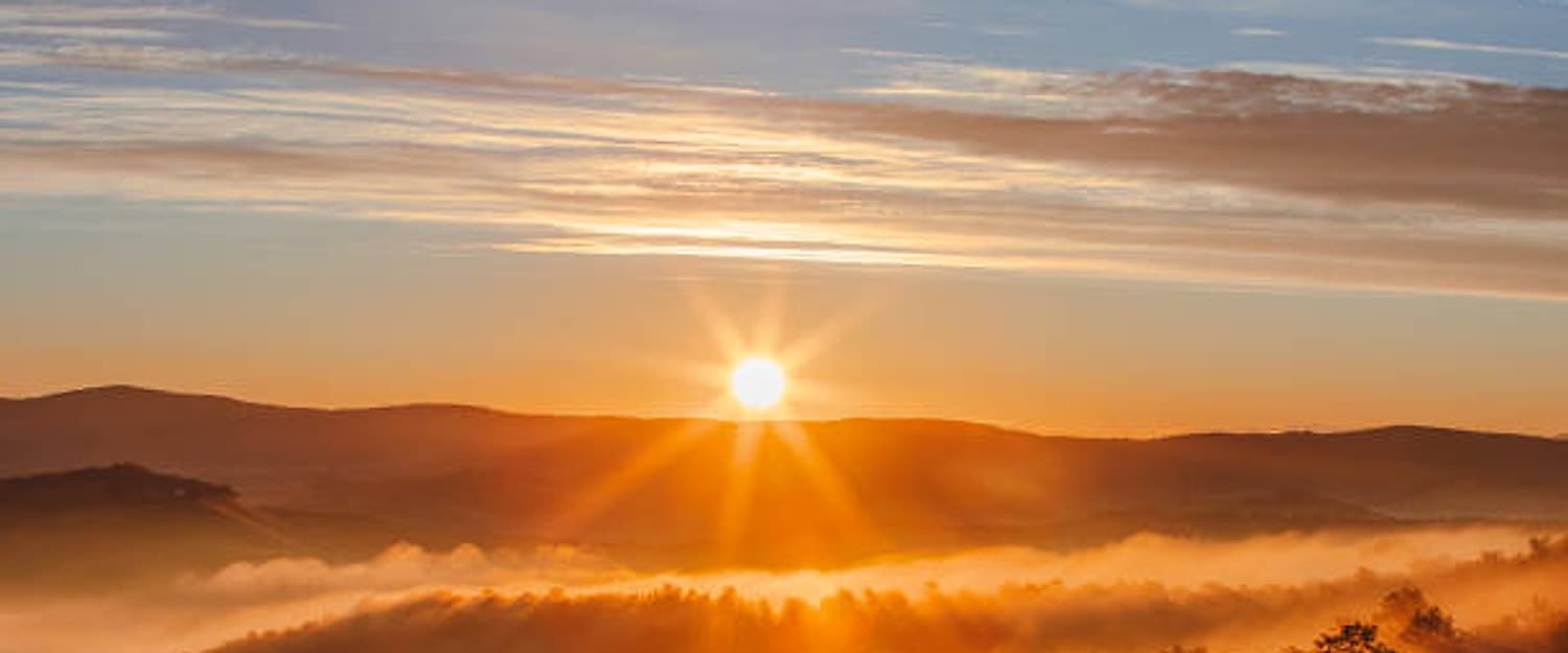 De zon die opkomt boven mistige heuvels